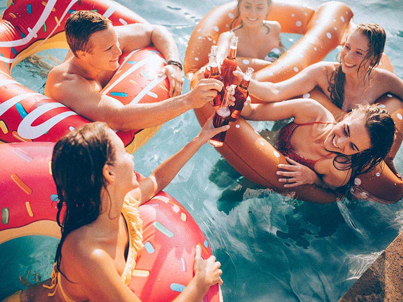 Friends celebrating summer in a pool with bottled beverages